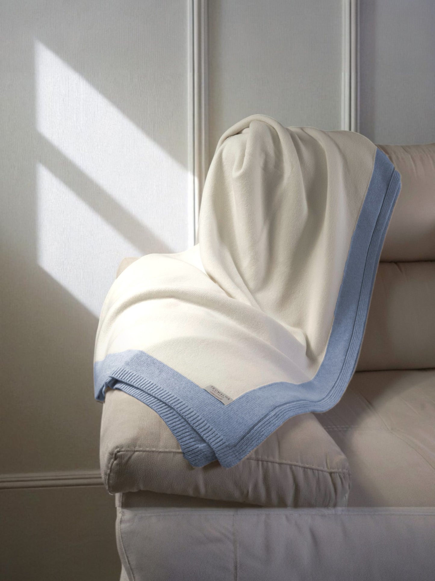 Two-tone wool blanket with a ribbed border, elegantly displayed on a sofa, showcasing its soft texture and neutral design.