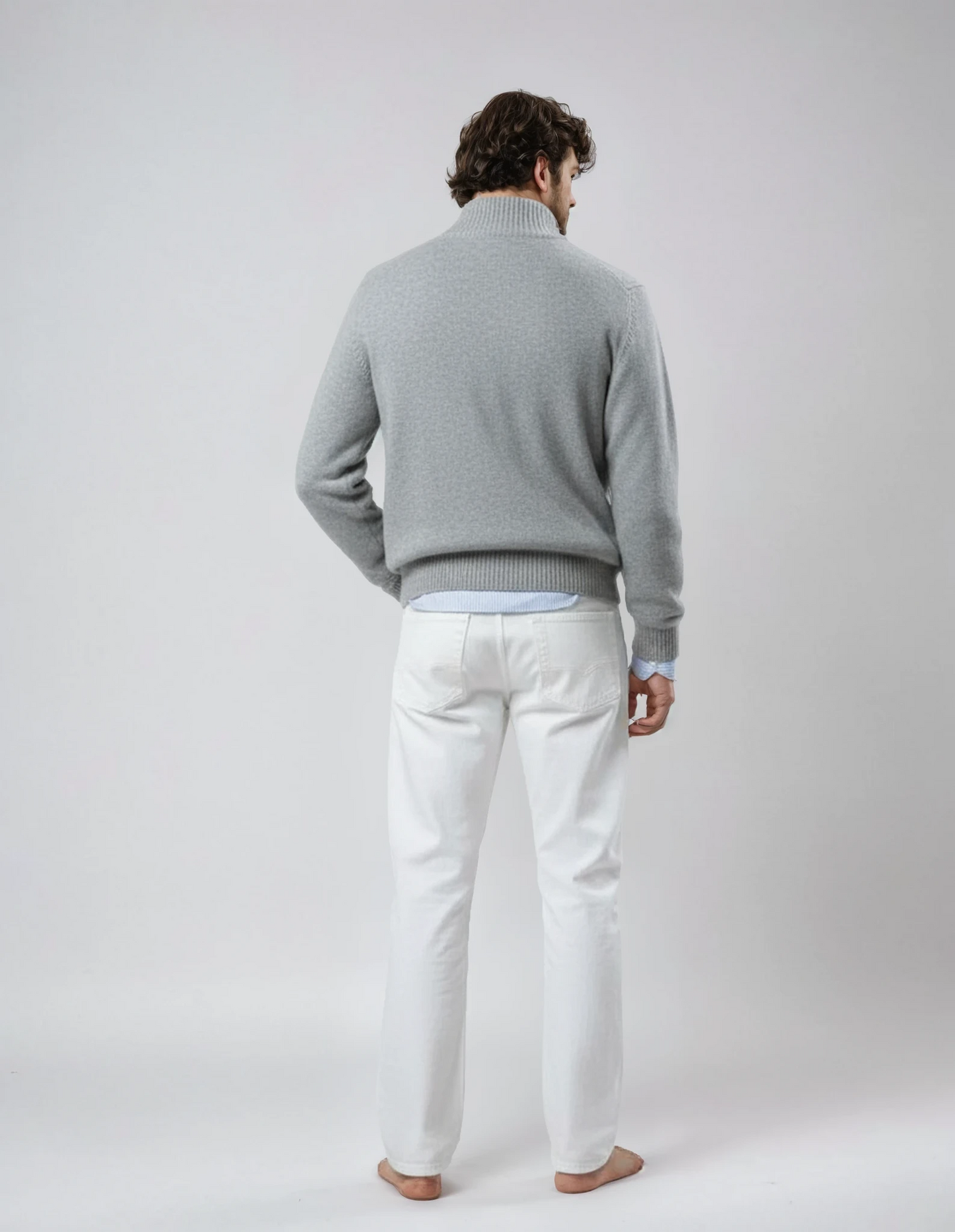 Rear view of a barefoot male model wearing a light gray wool jacket with front zipper and pockets, standing against a neutral background.