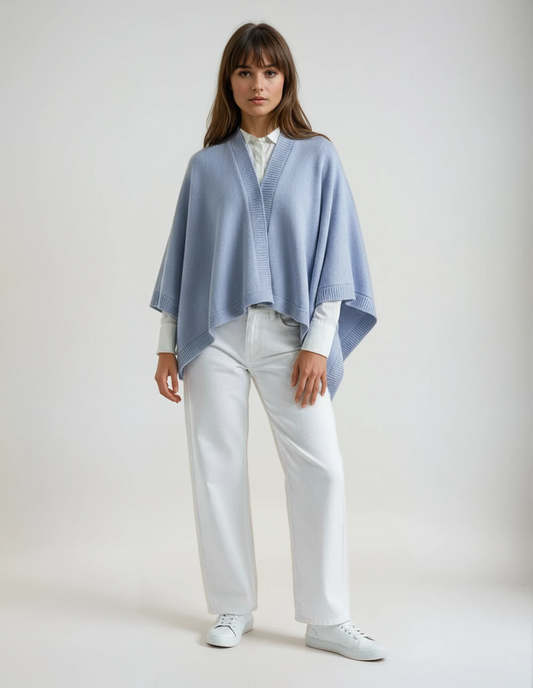 Woman wearing a baby blue cape over a white shirt and white pants, standing against a neutral background.