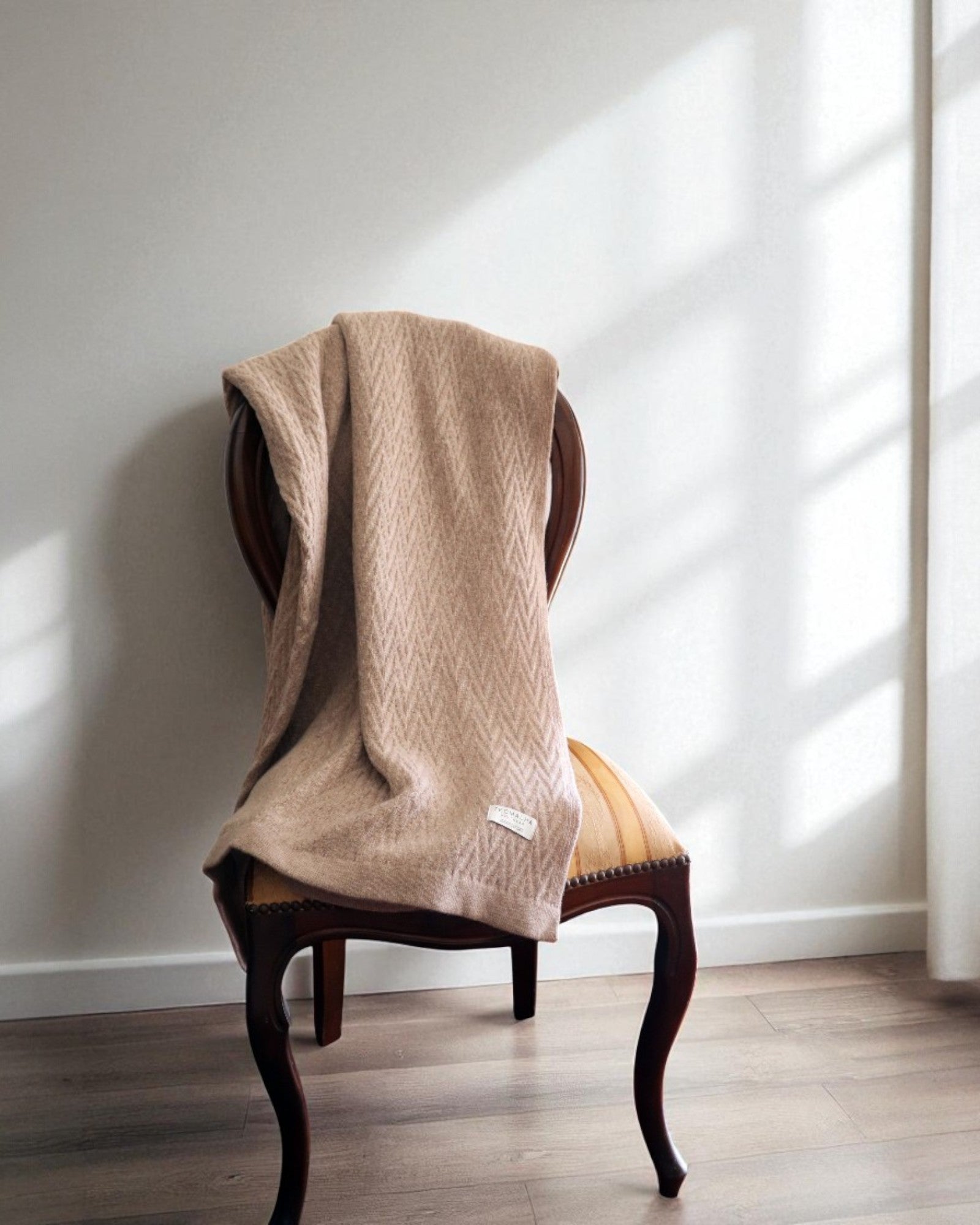 Beige herringbone wool blanket draped over a classic wooden chair in a minimalist room with natural light.