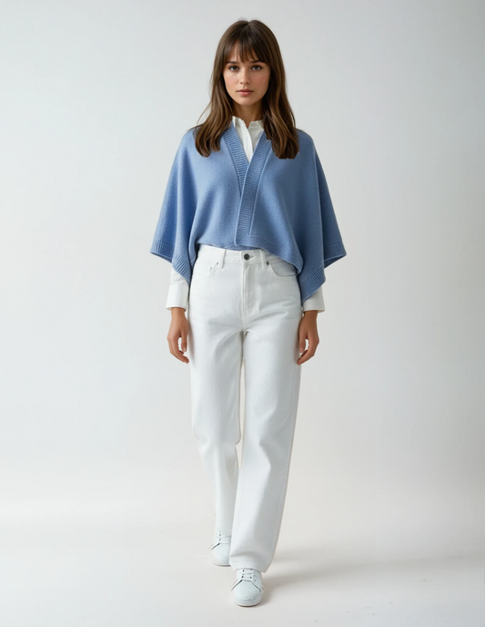 Woman wearing a lavender blue cape over a white shirt and white pants, standing against a neutral background.