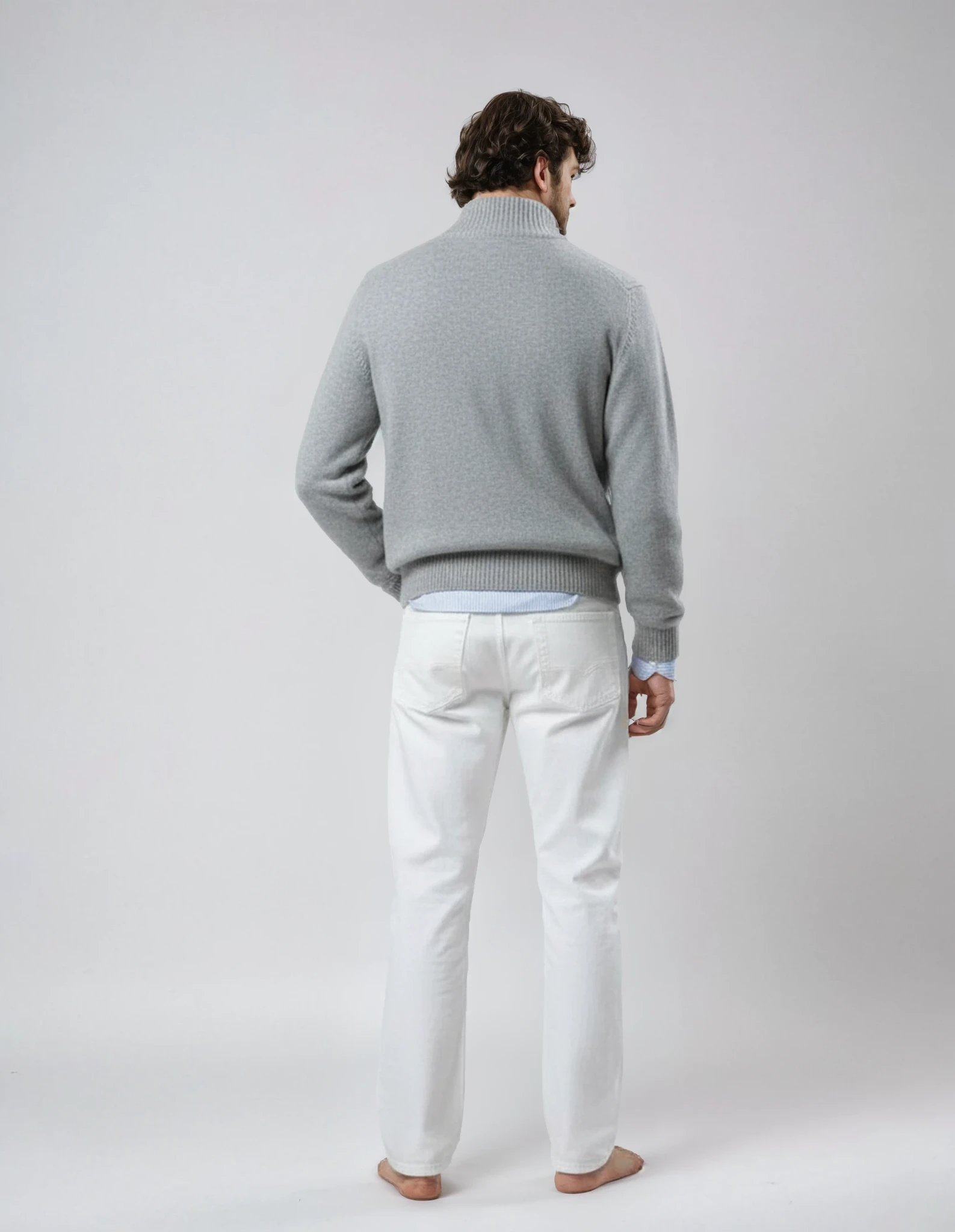 Rear view of a barefoot male model wearing a light gray wool jacket with front zipper and pockets, standing against a neutral background.