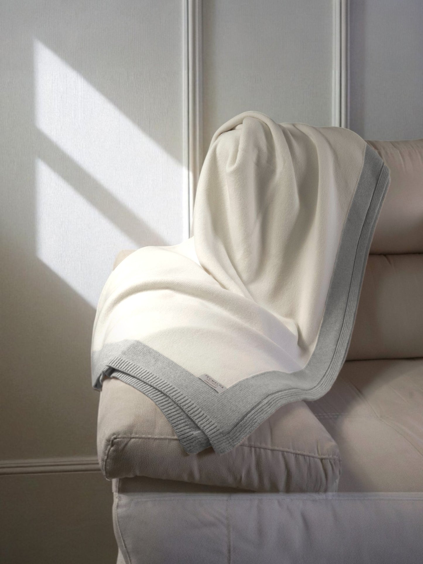 Two-tone wool blanket with a ribbed border, elegantly displayed on a sofa, showcasing its soft texture and neutral design.