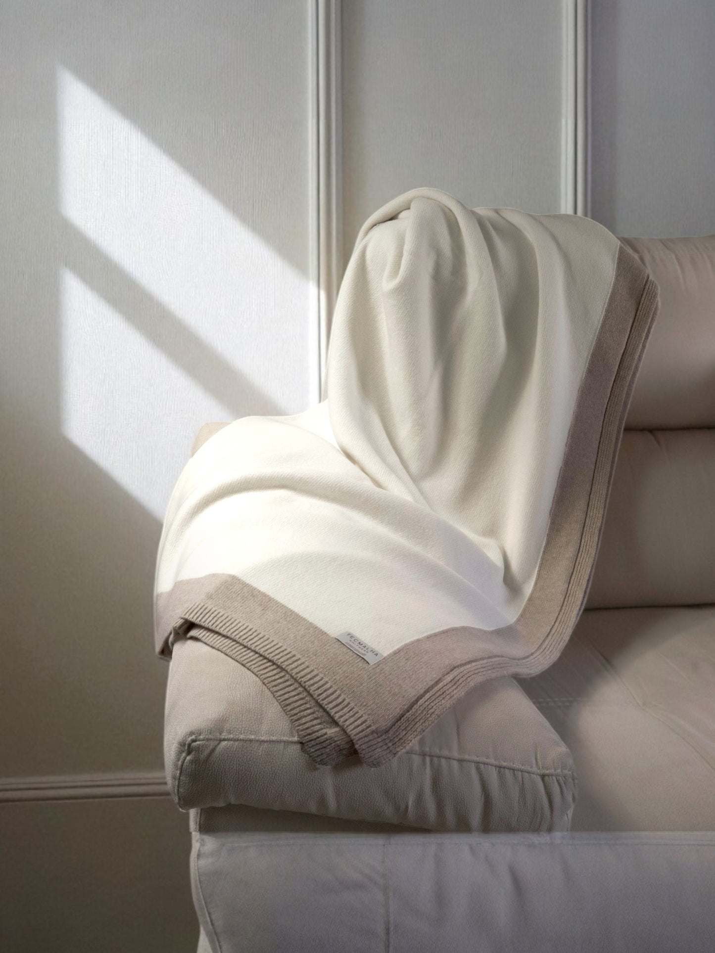 Two-tone wool blanket with a ribbed border, elegantly displayed on a sofa, showcasing its soft texture and neutral design.
