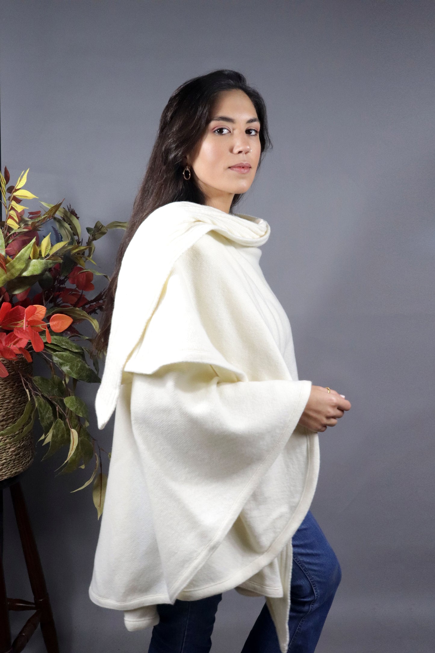 Woman seen from behind wearing a pearl hooded fall cape in a neutral setting with autumn leaves decoration.