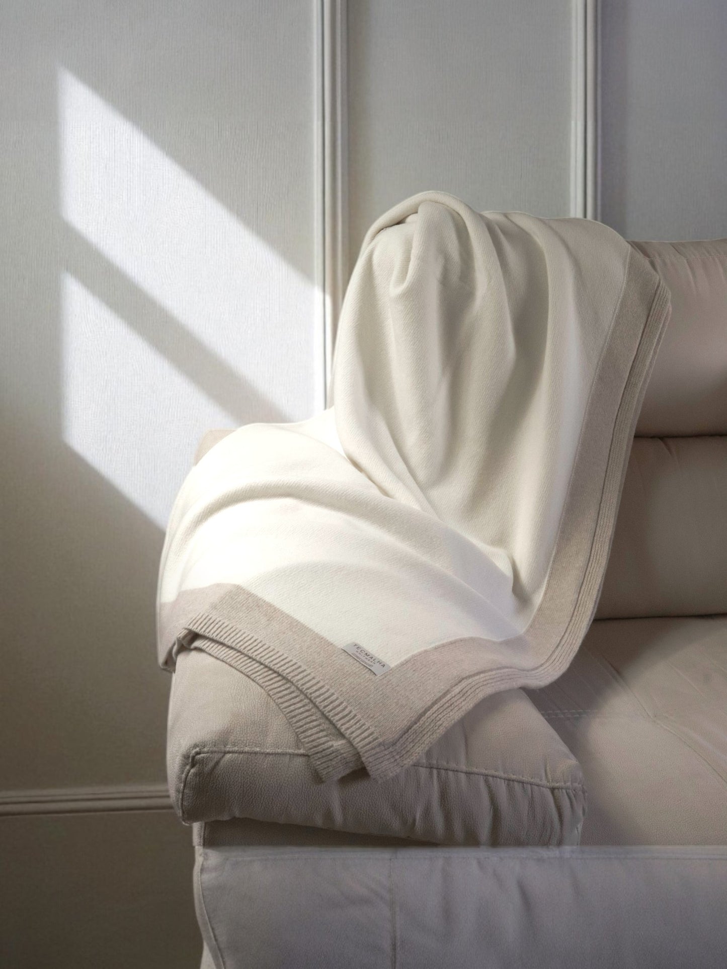 Two-tone wool blanket with a ribbed border, elegantly displayed on a sofa, showcasing its soft texture and neutral design.