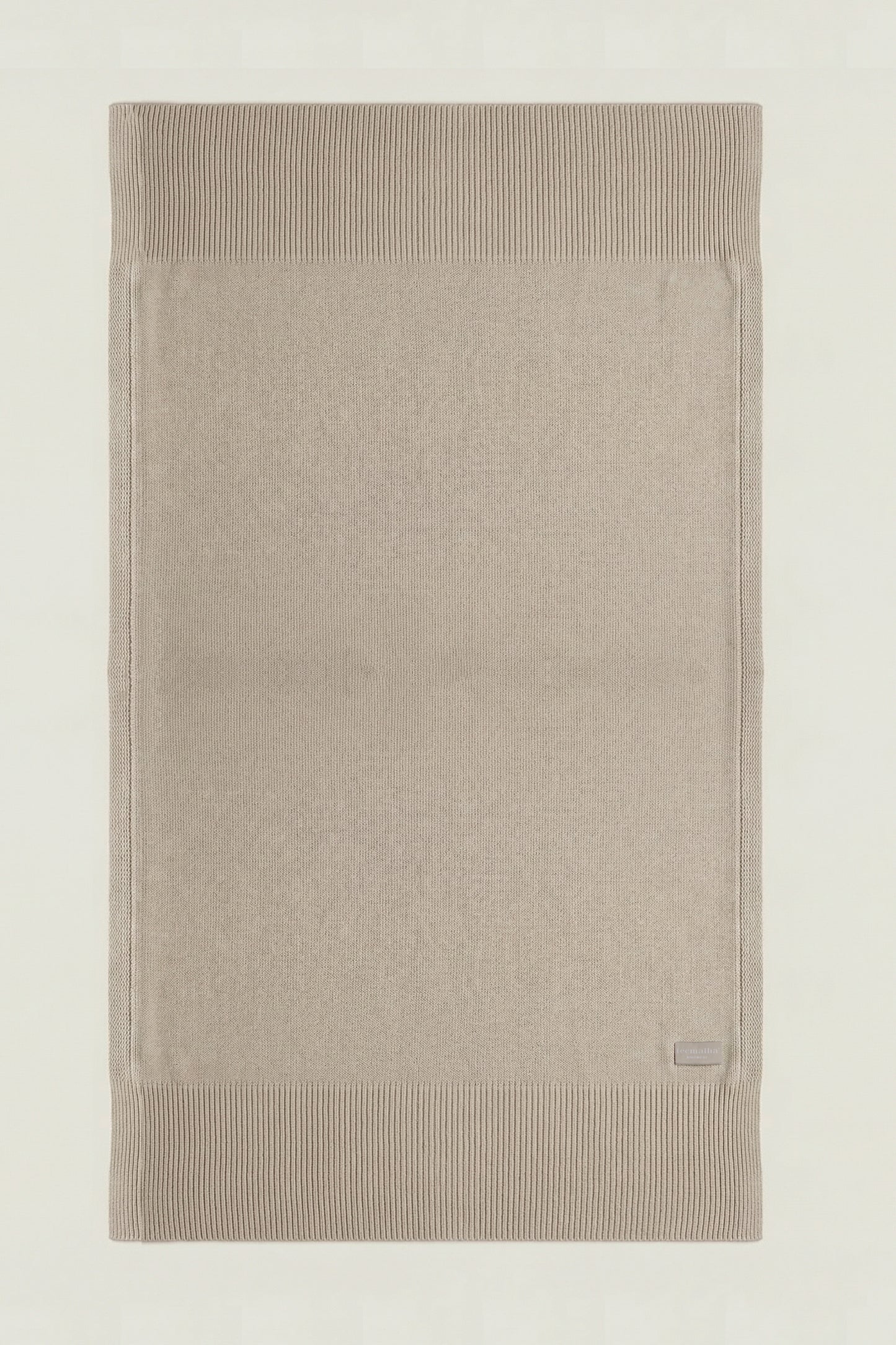 Top-down view of a rectangular cotton knit throw in beige, showing the full design and structured borders.