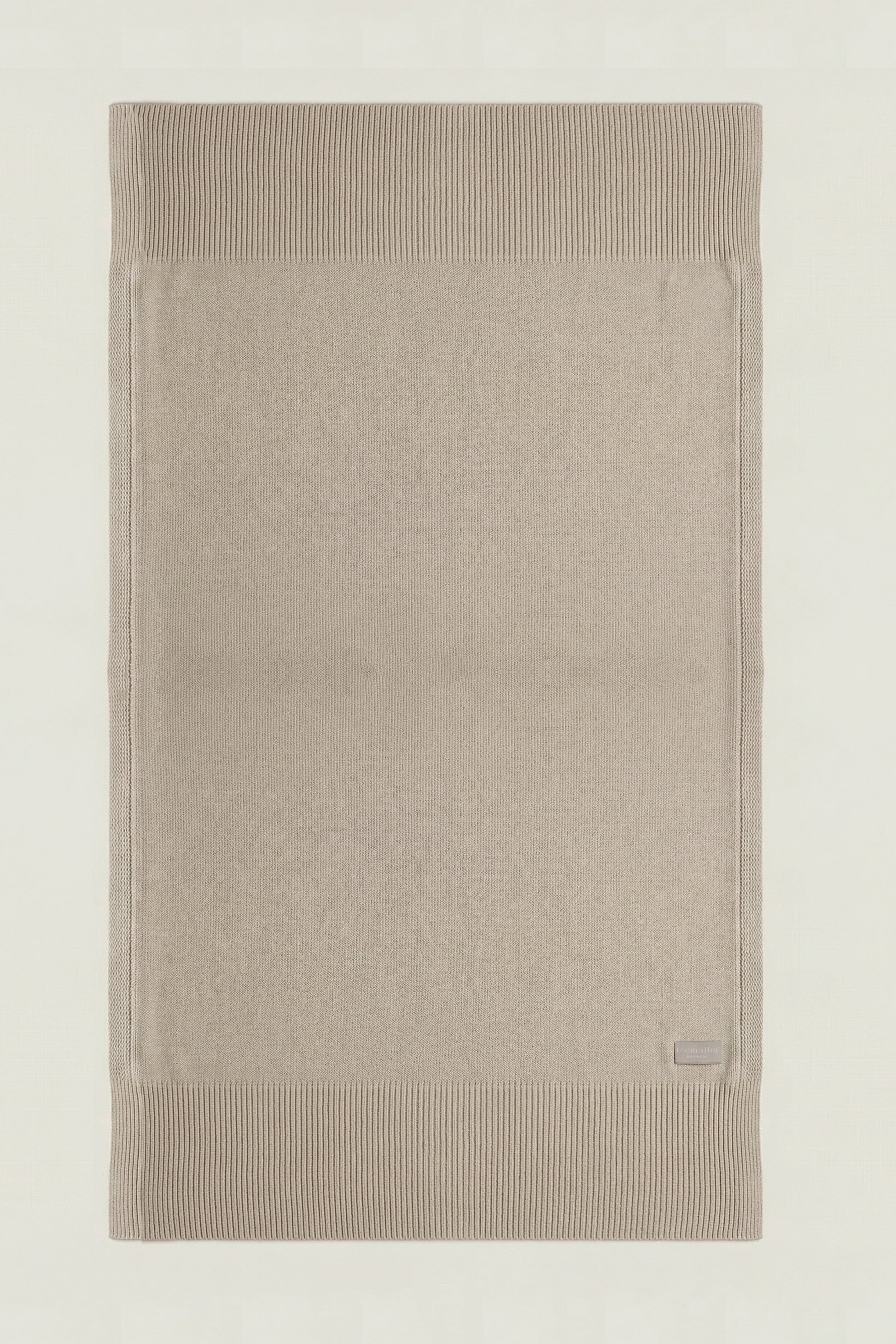 Top-down view of a rectangular cotton knit throw in beige, showing the full design and structured borders.