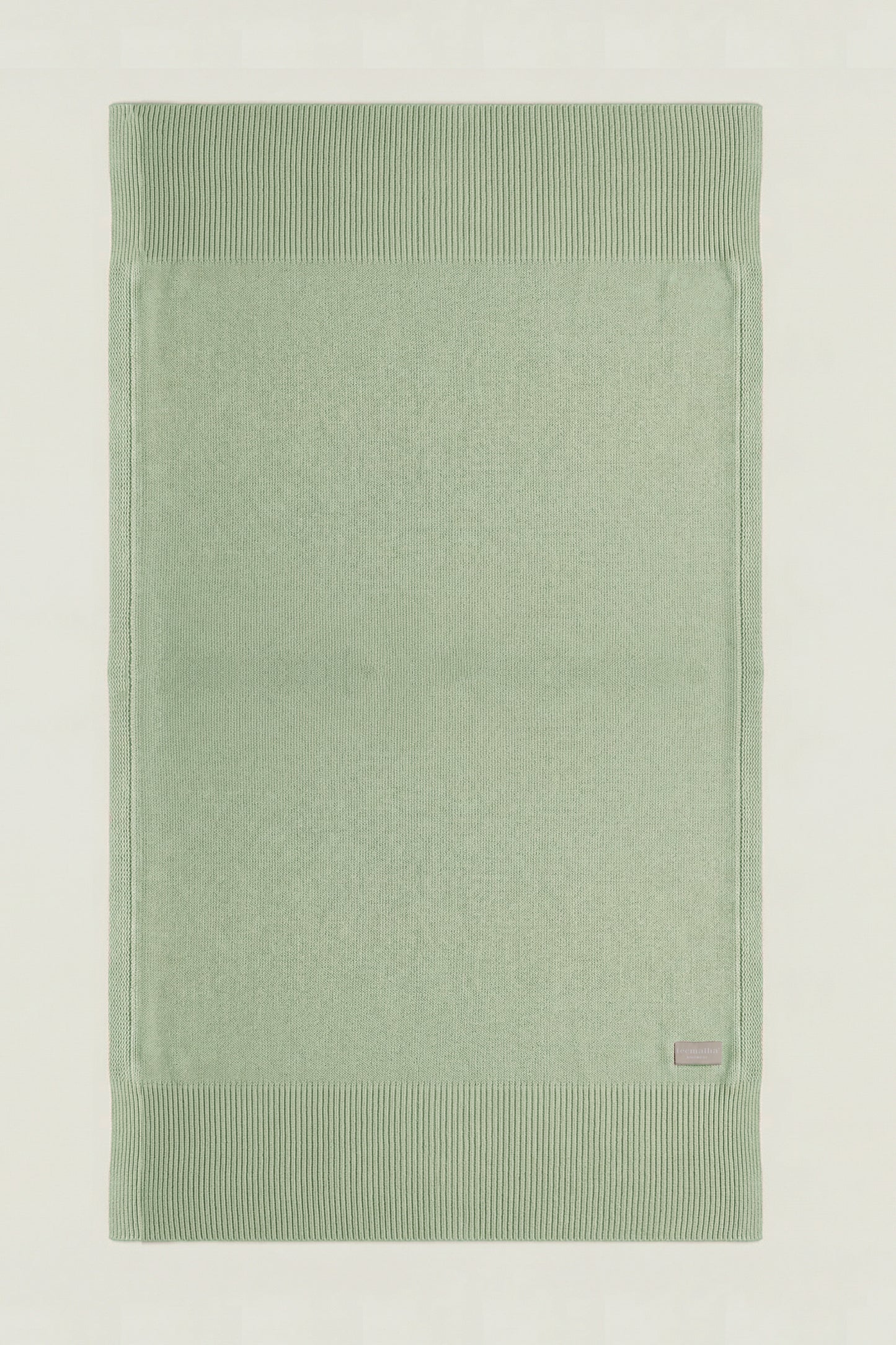Top-down view of a rectangular cotton knit throw in green showing the full design and structured borders.