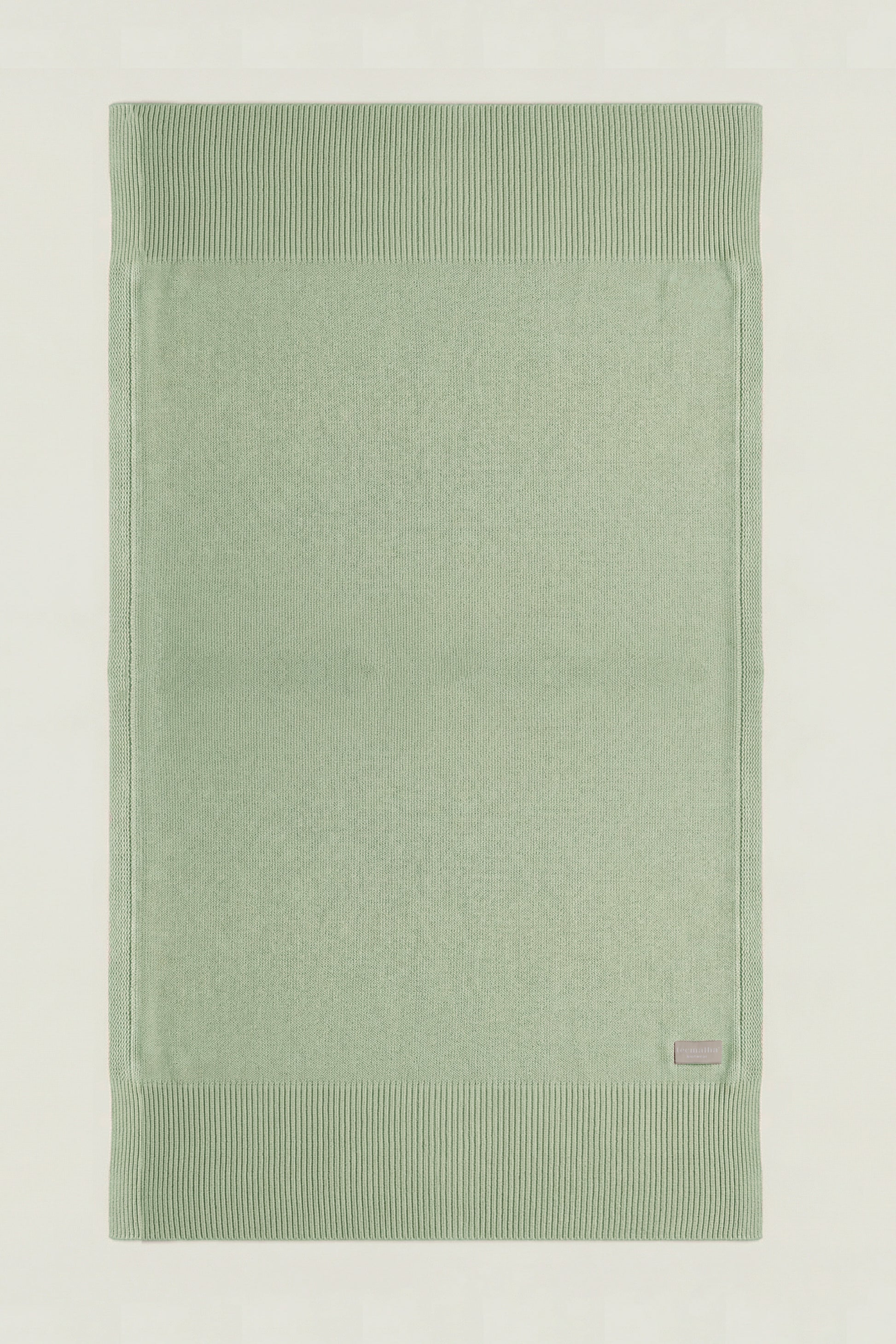 Top-down view of a rectangular cotton knit throw in green showing the full design and structured borders.