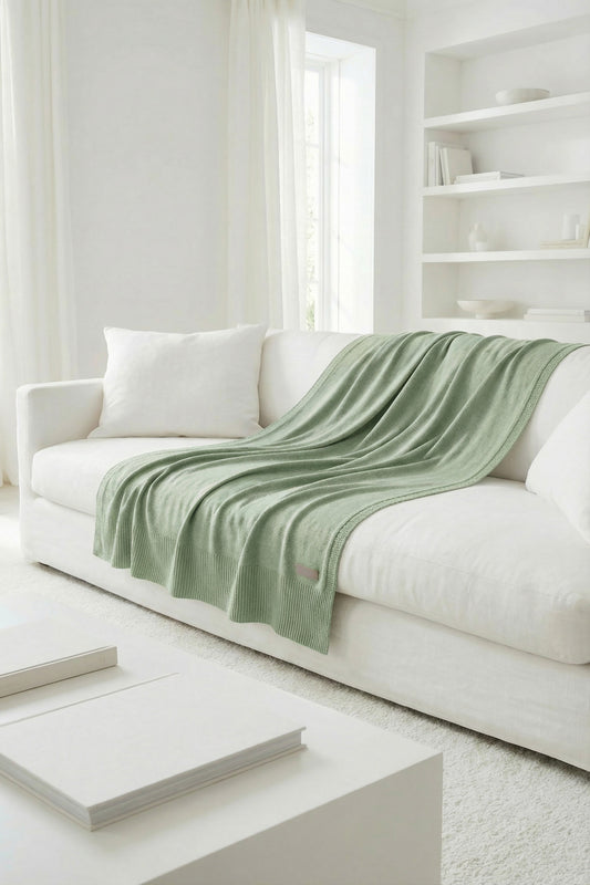 Sage green cotton knit blanket on a white sofa in a bright, modern living room.