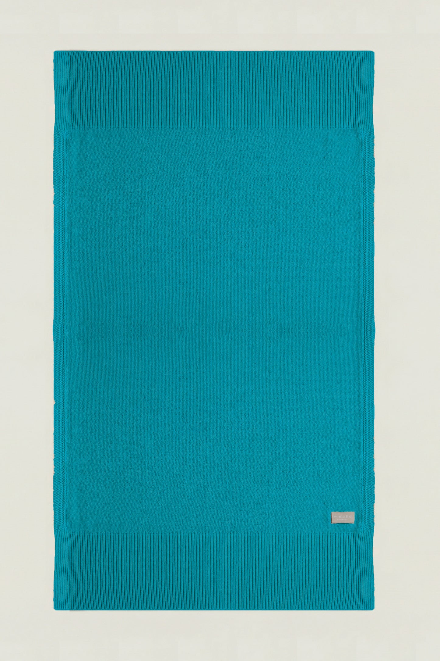 Top-down view of a rectangular cotton knit throw in ocean green, showing the full design and structured borders.