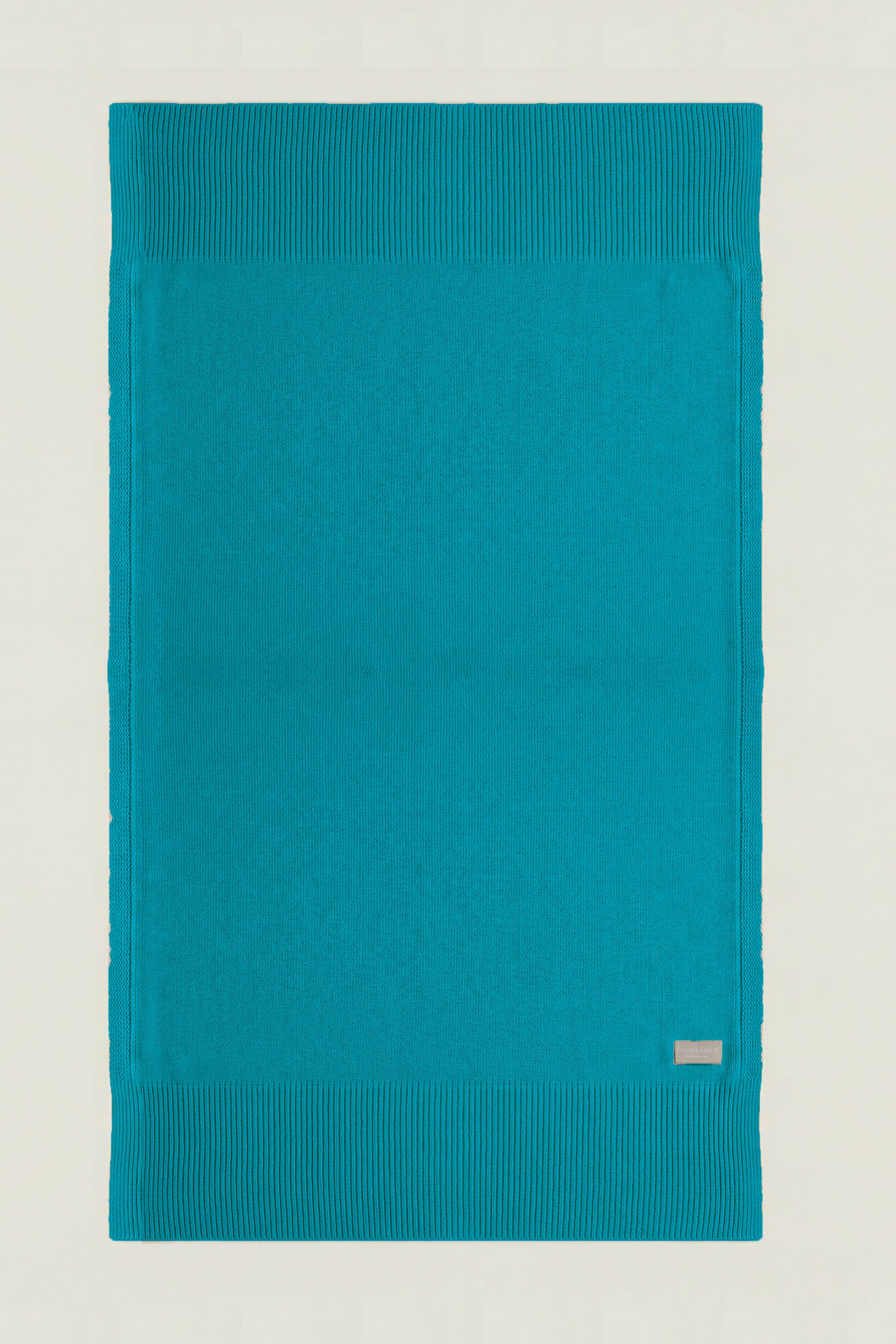 Top-down view of a rectangular cotton knit throw in ocean green, showing the full design and structured borders.