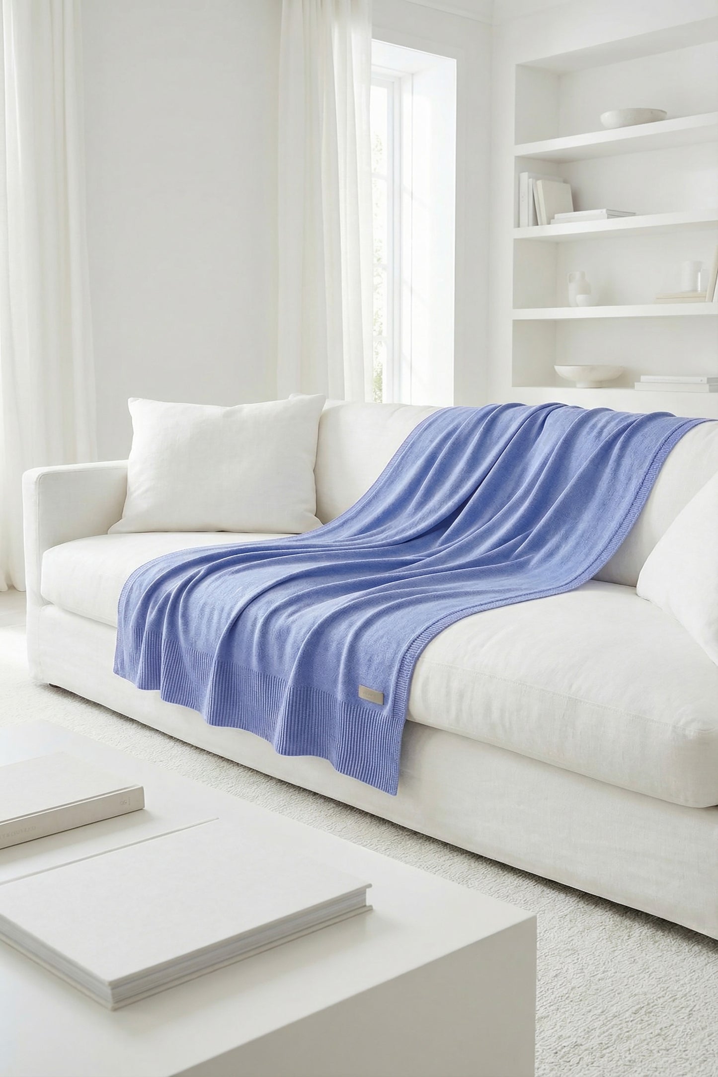 Minimalist pastel blue cotton knit throw draped on a white sofa, showcasing a ribbed border and soft texture.