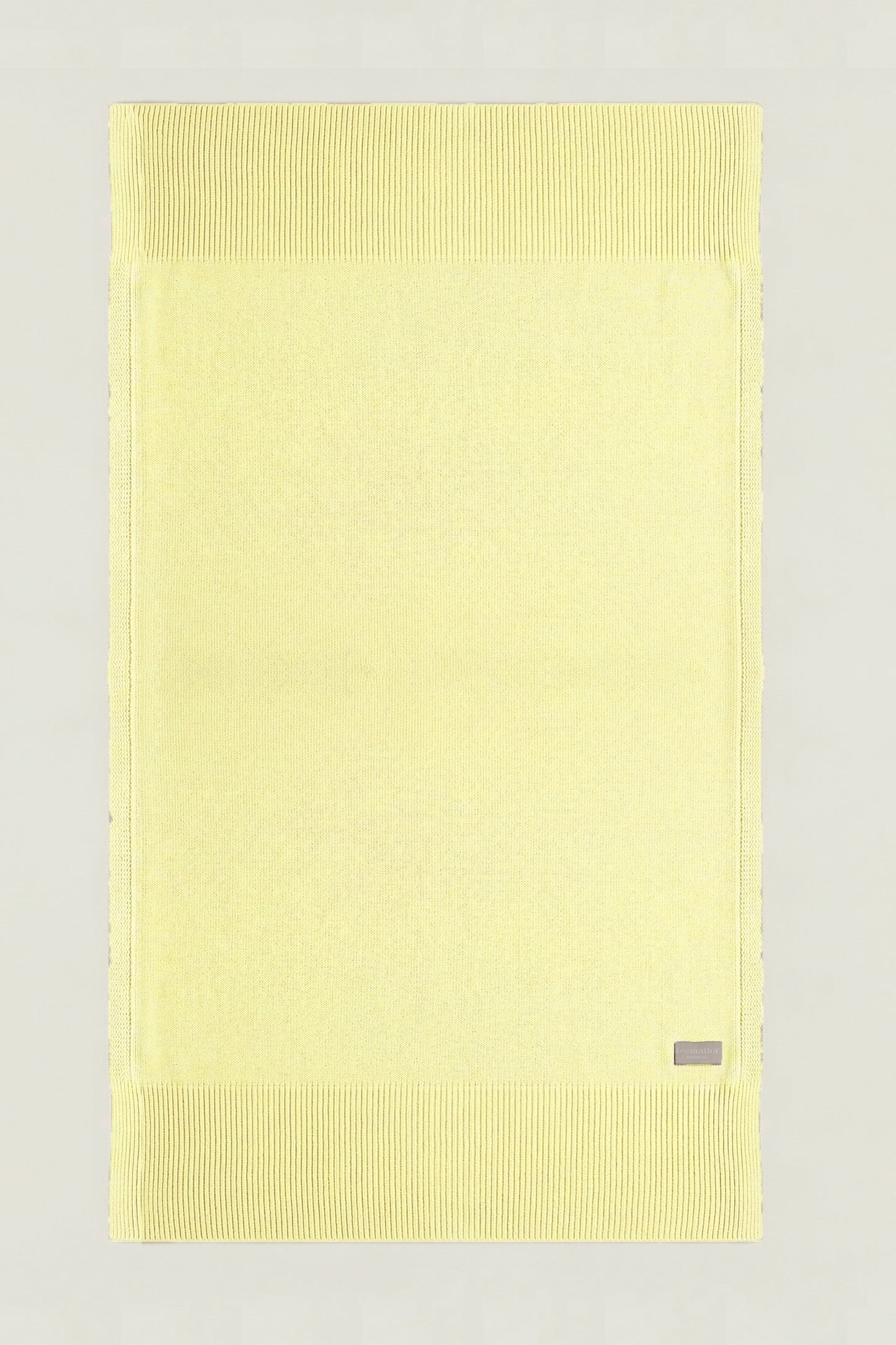 Top-down view of a rectangular cotton knit throw in yellow, showing the full design and structured borders.