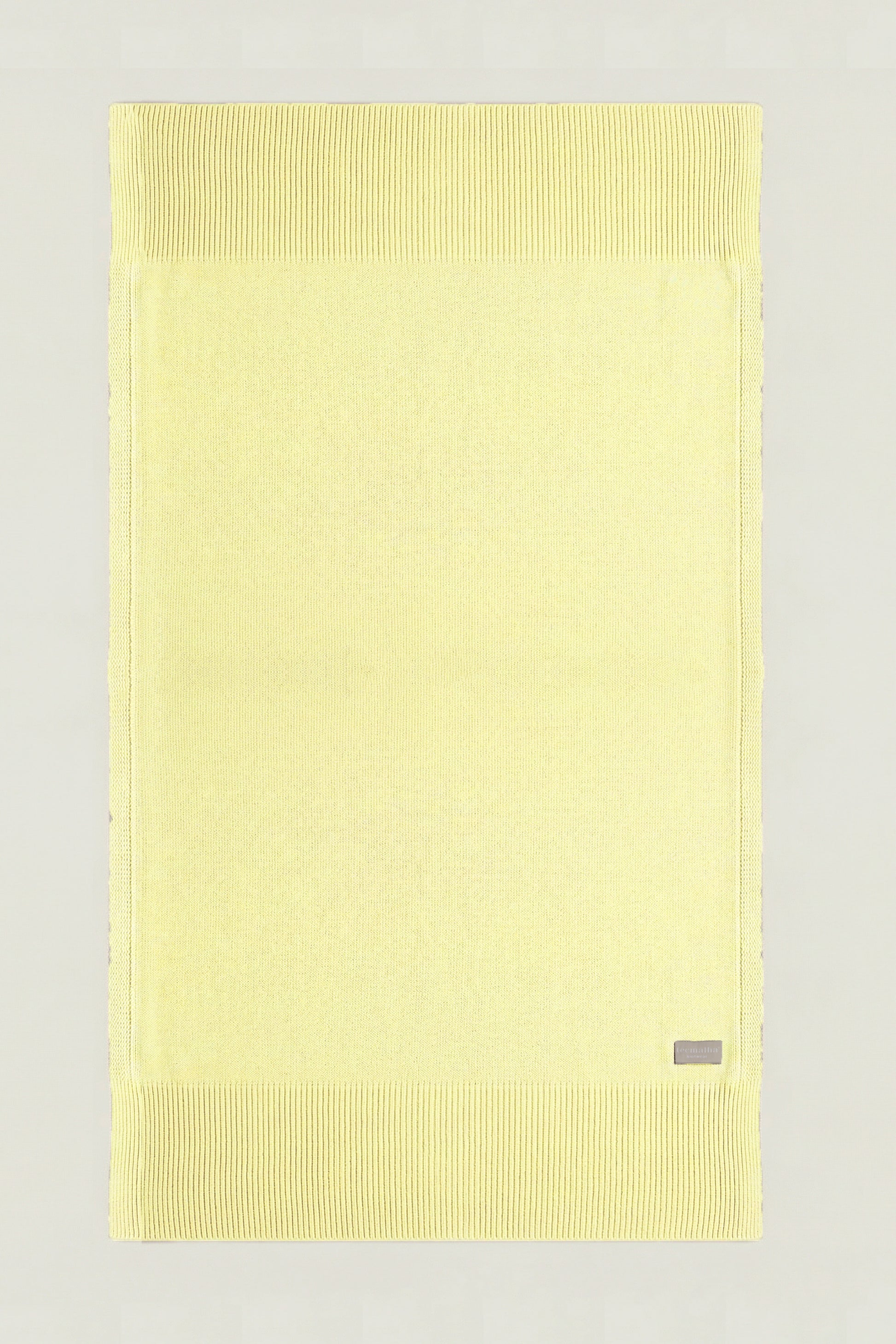 Top-down view of a rectangular cotton knit throw in yellow, showing the full design and structured borders.