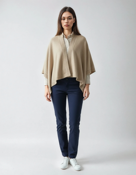 Woman wearing a sand-colored cape over a white shirt and blue pants, standing against a neutral background.