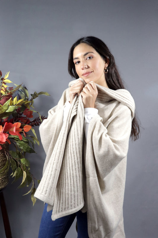 Woman seen from behind wearing a sand hooded fall cape in a neutral setting with autumn leaves decoration.