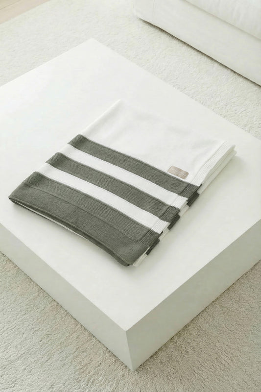 Square-folded white knit blanket with moss green stripes on a clean white pedestal.