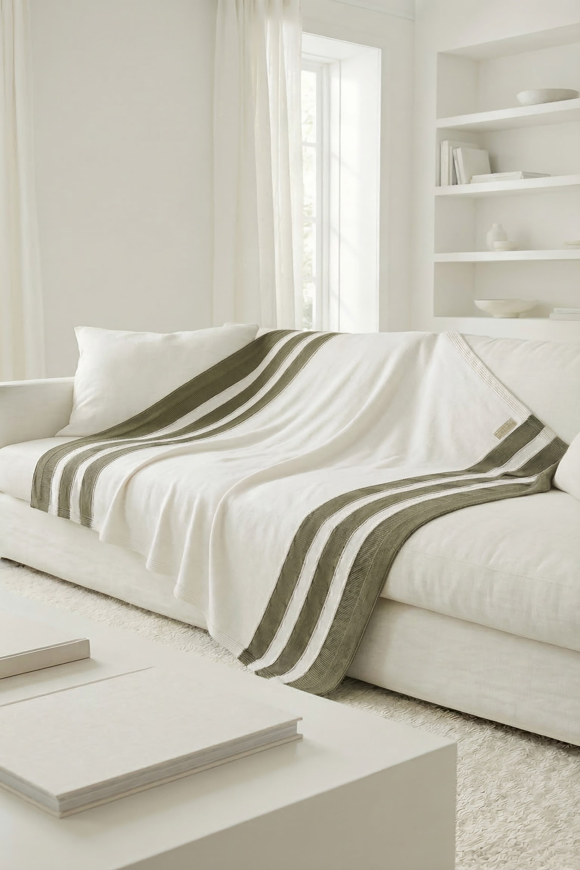 White knit blanket with moss green stripes draped over a sofa, highlighting the natural and earthy tones.