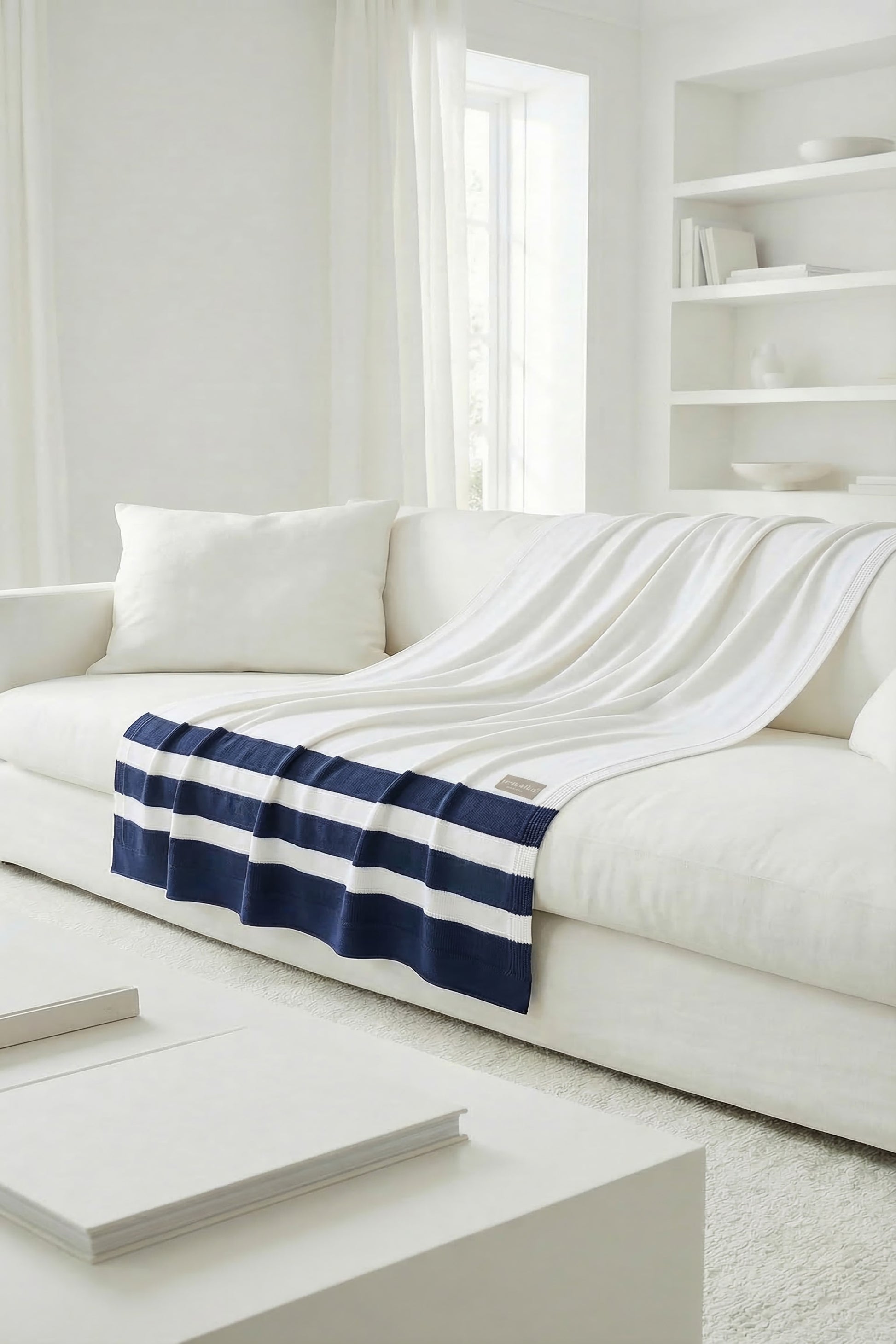 Striped knit throw blanket in white and navy blue spread on a sofa, focusing on the elegant drape at the edge.