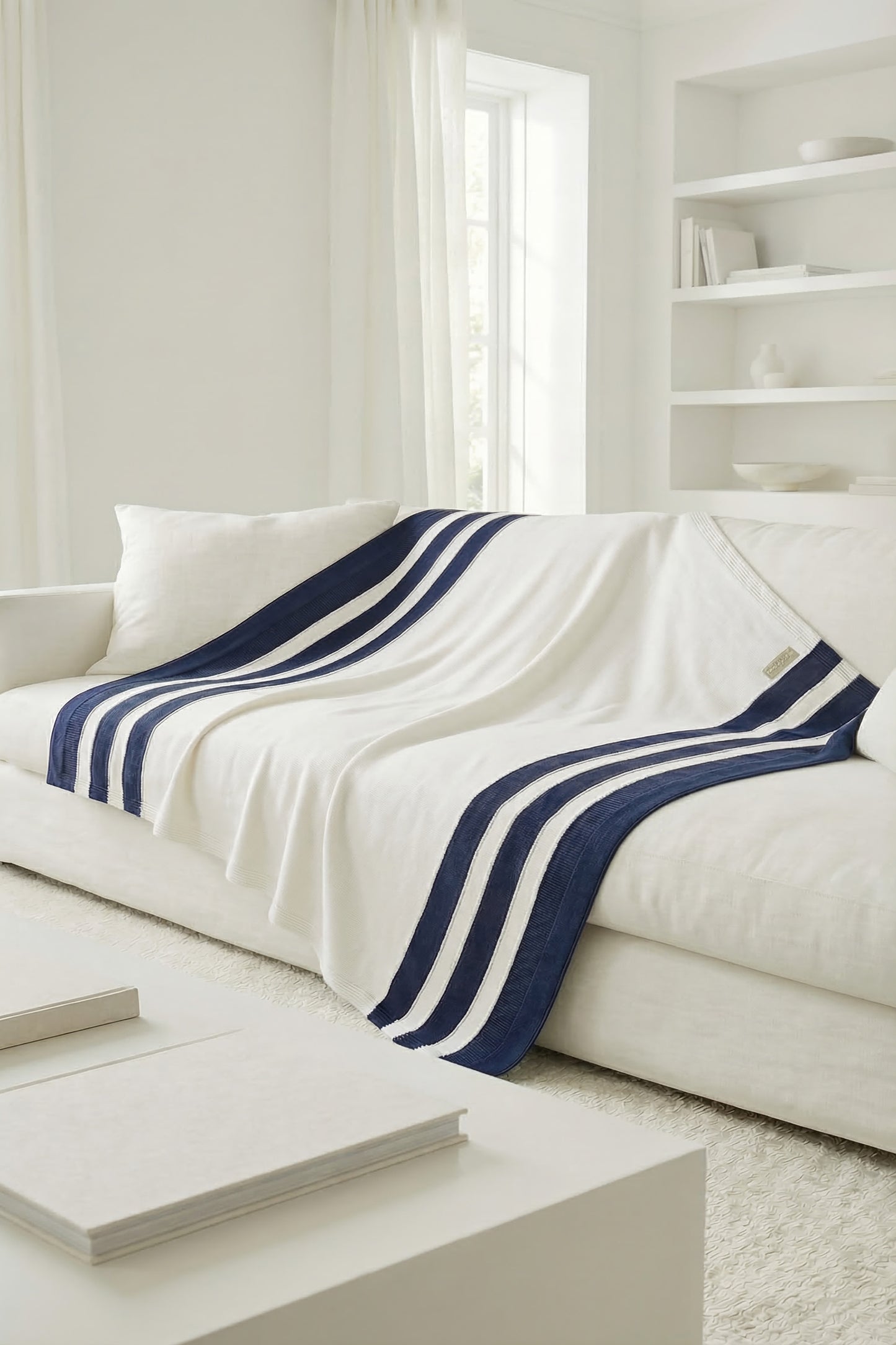White knit cotton blanket with three navy blue stripes draped over the back and seat of a white sofa.