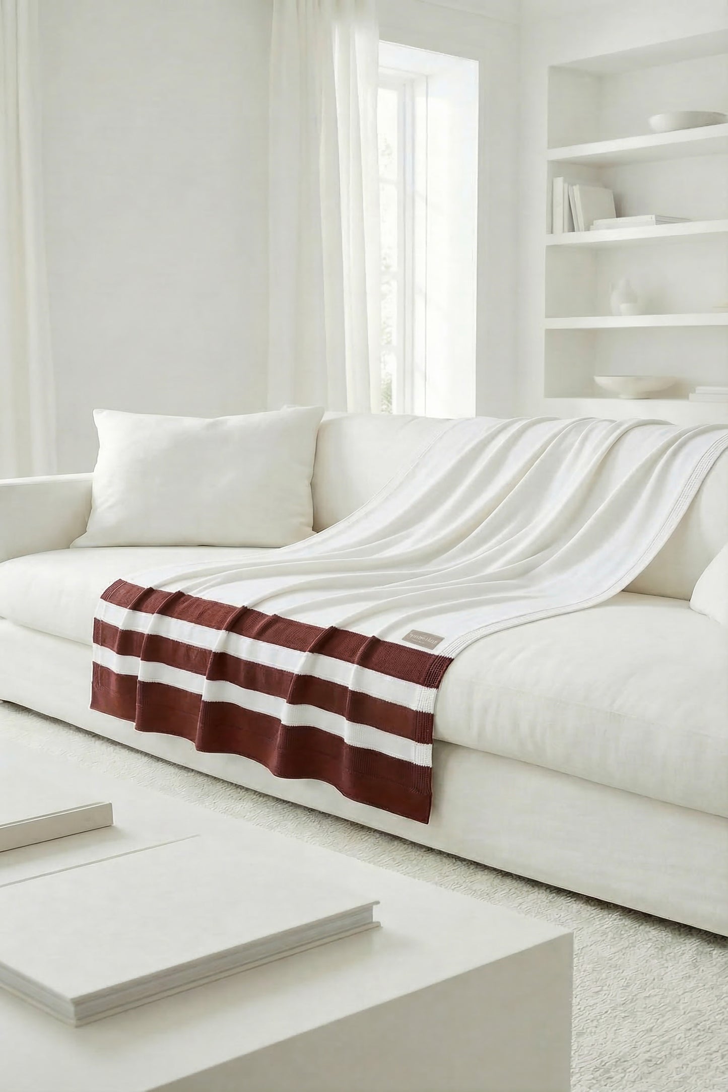 White knit throw with terracotta stripes on the front edge, displaying a soft and natural drape on the sofa.