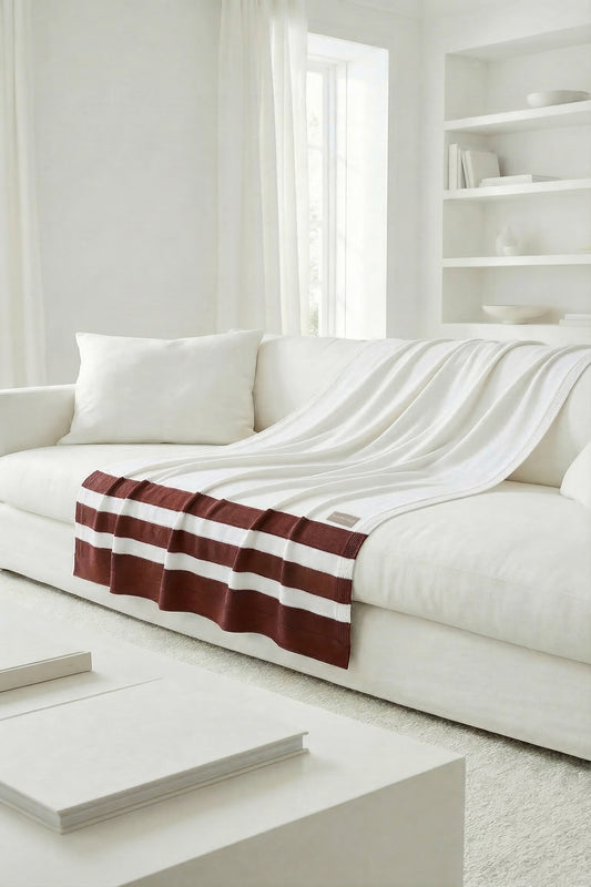 White knit throw with terracotta stripes on the front edge, displaying a soft and natural drape on the sofa.