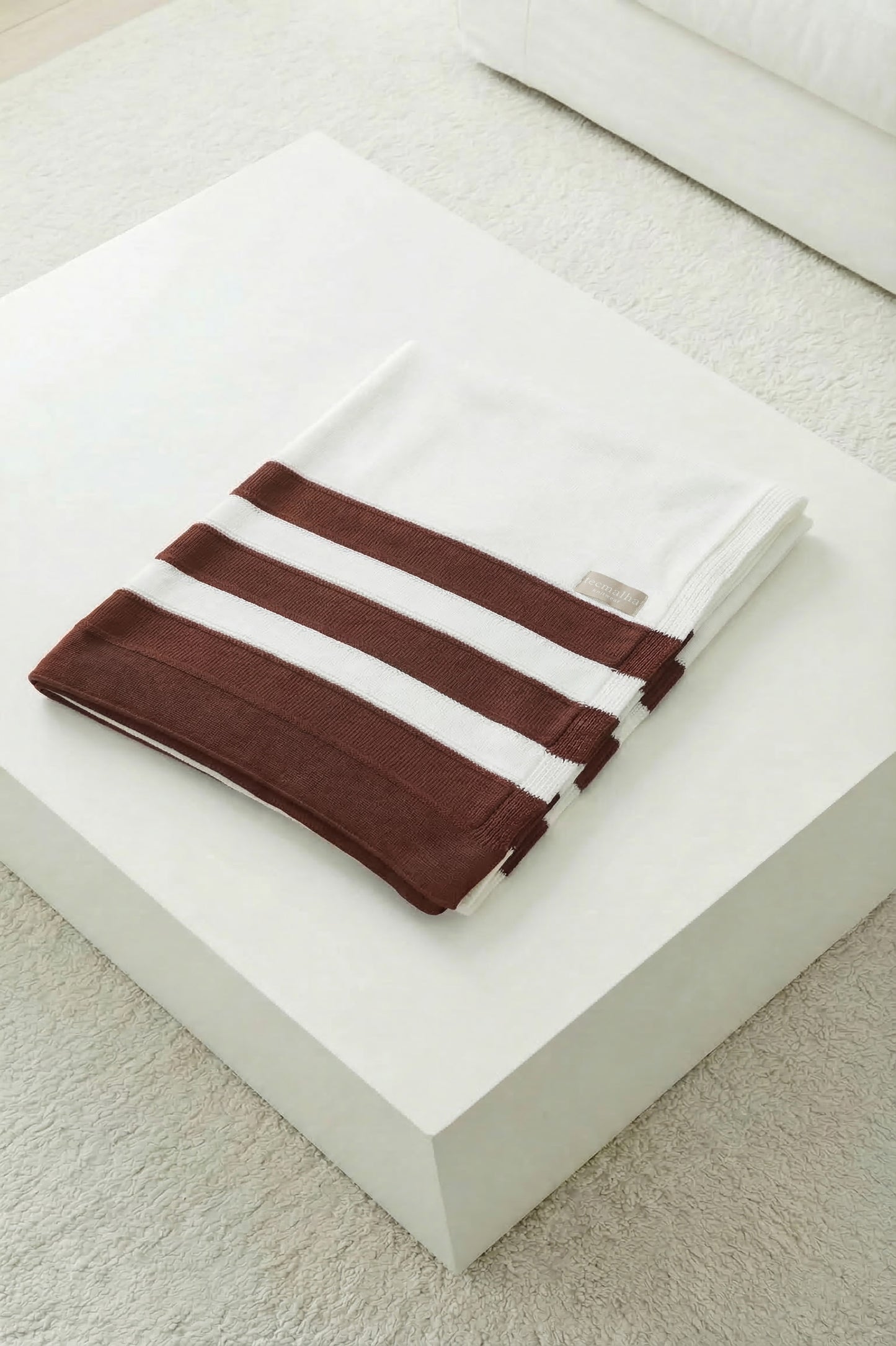 Neatly folded white knit blanket featuring three terracotta stripes on a white minimalist background.