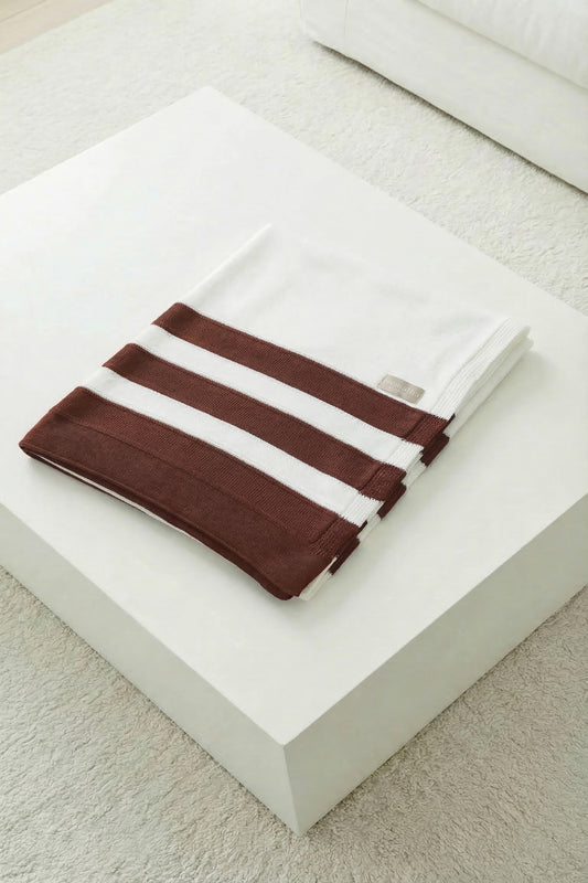Neatly folded white knit blanket featuring three terracotta stripes on a white minimalist background.