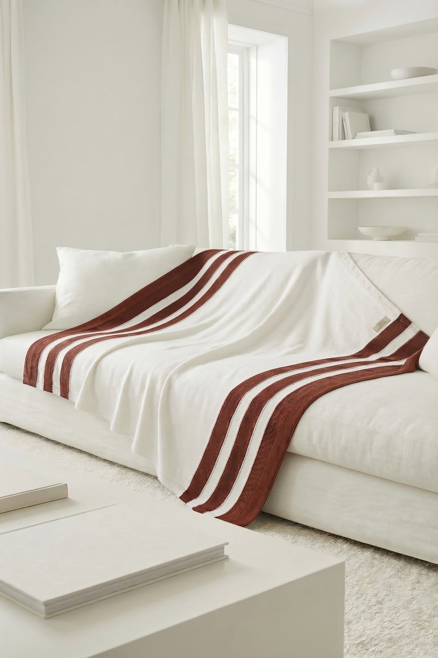 White cotton knit blanket with terracotta orange stripes spread across the top of a modern white sofa.