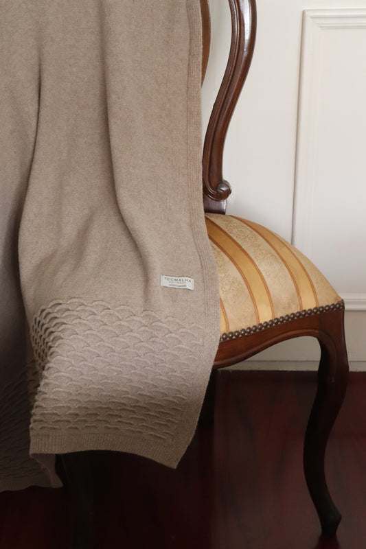 Close-up view of a beige wool blanket with a raised wave pattern detail on the edges.